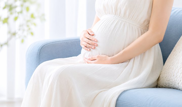 ソファでお腹に手を添える妊娠中のママ